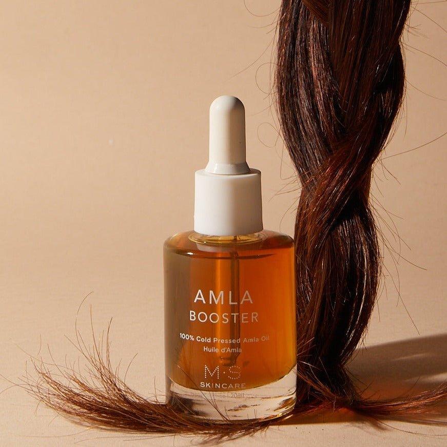 M.S Skincare AMLA OIL for face & body-frosted luxury white bottle,dropper and printing on top of a braid on a beige backdrop.