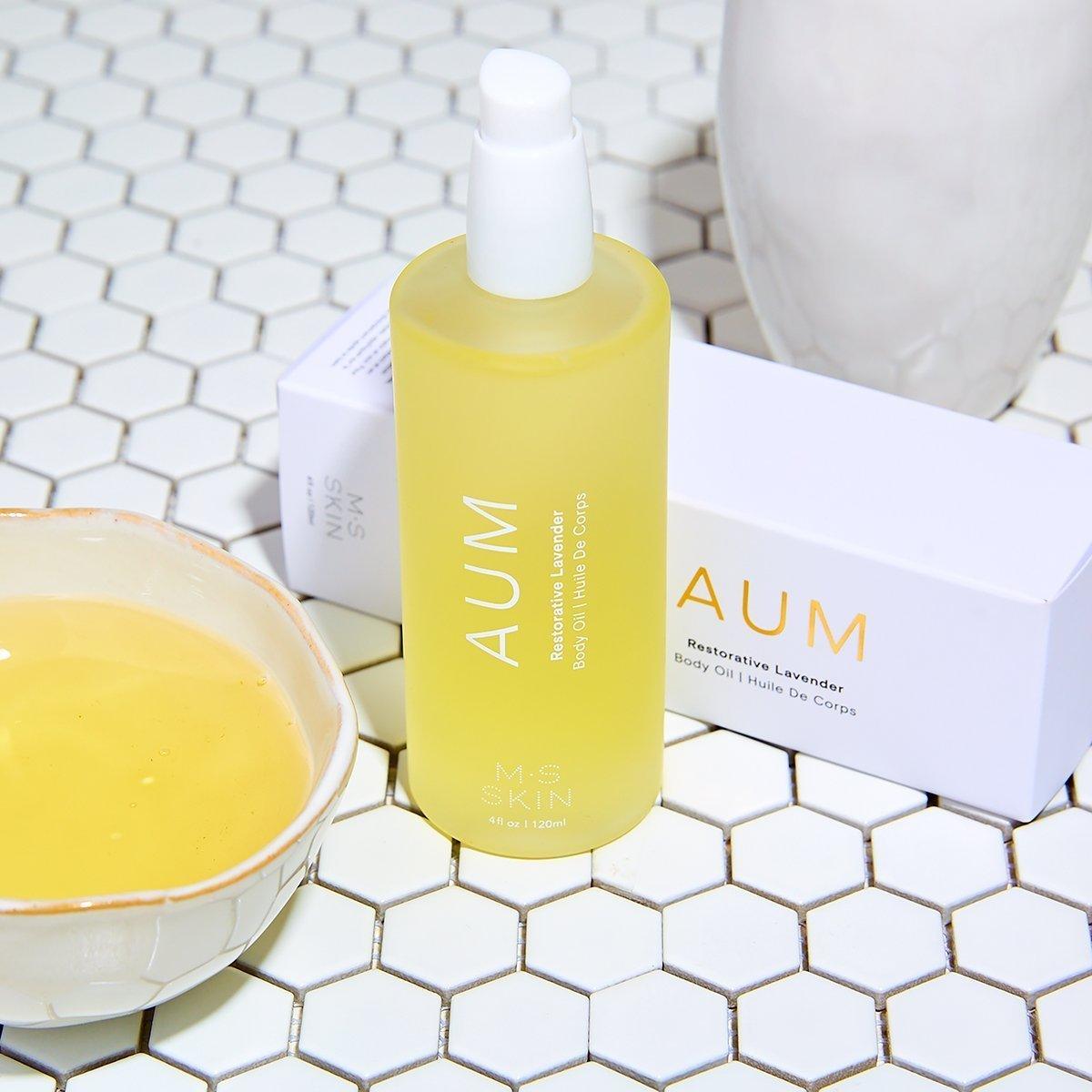 M.S Skincare AUM Lavender Restorative Body Oil -luxury skincare in a white bottle on a tile background with a bowl of oil.