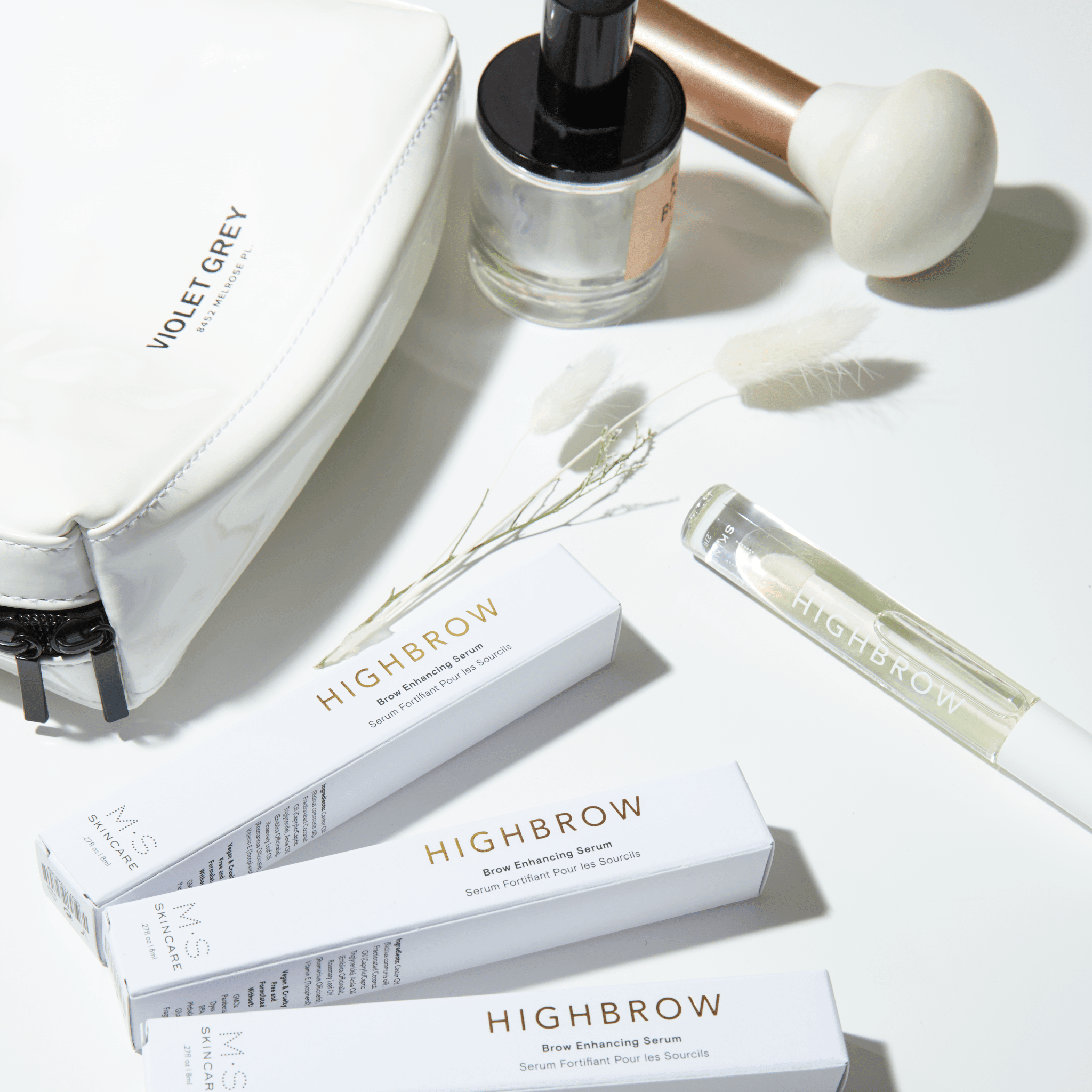 M.S Skincare HIGHBROW Brow Enhancing Serum in a glass container with white wand and cap with other makeup items.